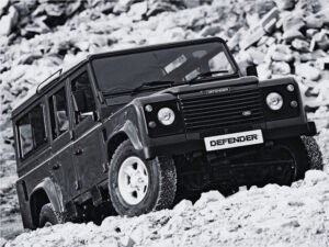 A vintage Defender with a matte black finish, roof rack, and LED light bar, ready for an off-road expedition.