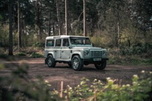 A vintage Defender retrofitted with an electric powertrain, driving silently through a forest trail.